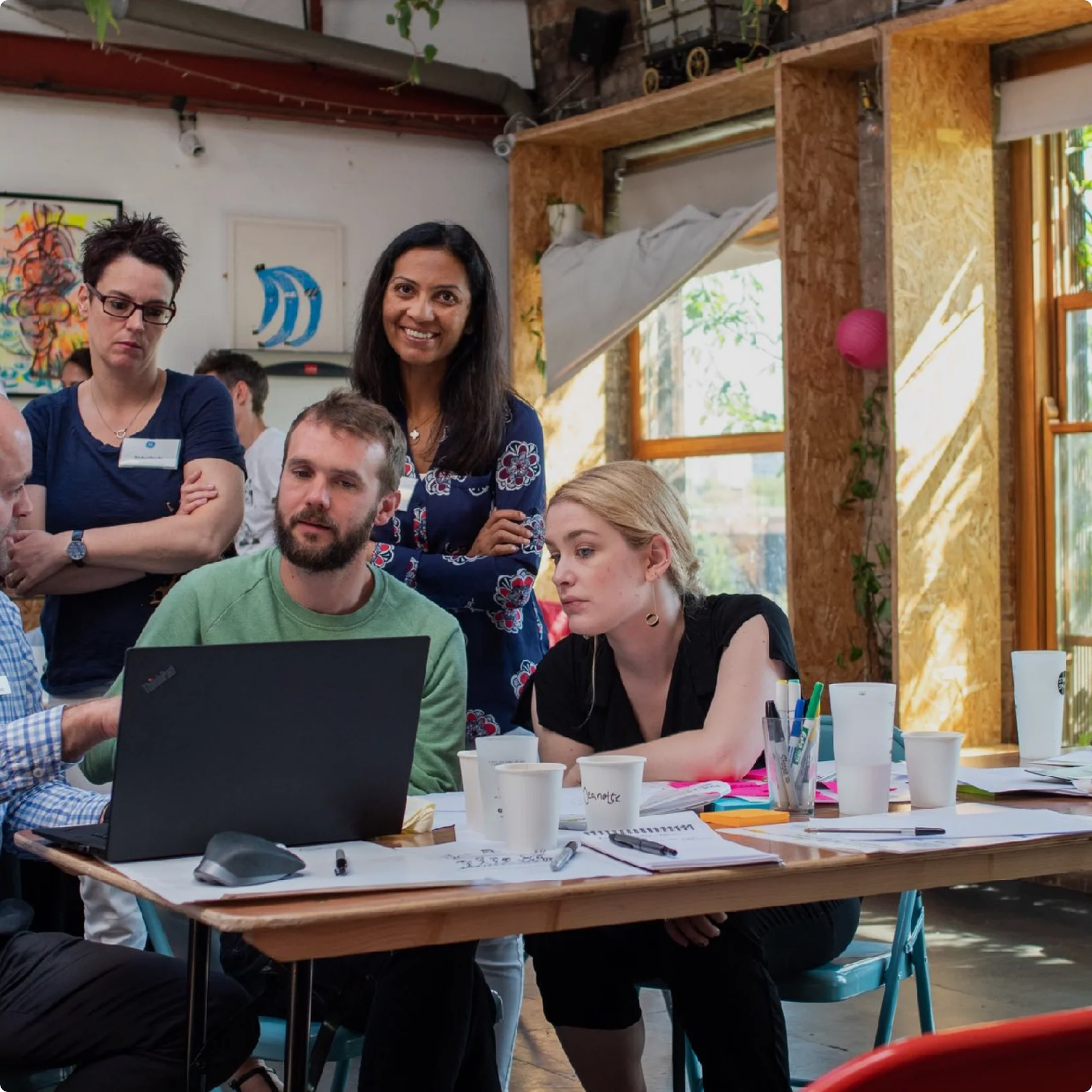 One of the directors around multiple people showing something to them on a laptop